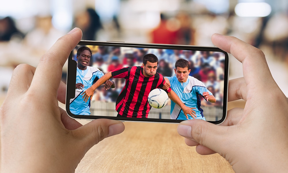 Close-up of hands holding a smartphone with a soccer/football game playing