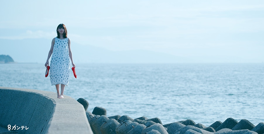 a woman walks along a sea wall in a still from the movie three trees