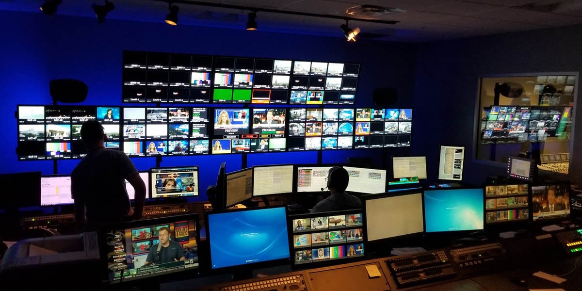 Newsroom with numerous monitors, editing stations and two men working